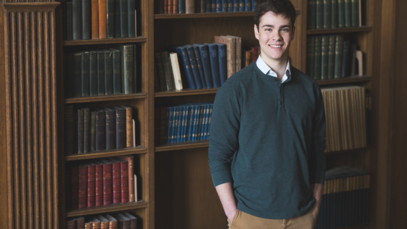 Landscape - Alex Joel in front of a wooden book case in the tower room on Dartmouth Campus