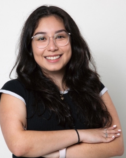 A smiling girl wearing glasses is posed in front of a blank background.