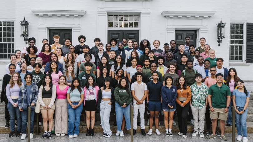 A group of students gathered on a set of steps, smiling warmly for a group photo. They are arranged in rows.