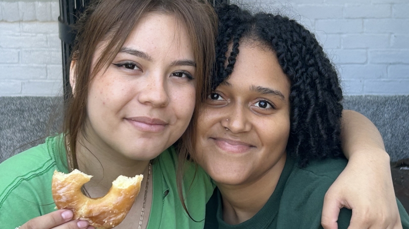 Two girls smiling and posed in front of the camera while one of them hold up a donut.