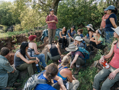 Students listen to a presentation in a field.
