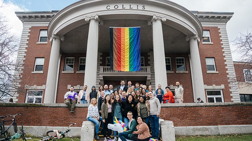 Collis staff pose outside of Collis Hall in front of the pride flag.