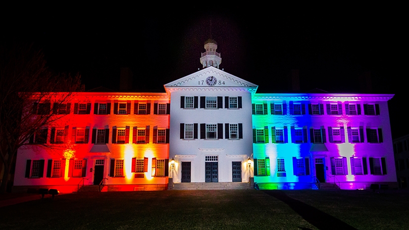 dartmouth hall showcased and illuminated with red, orange, yellow, green, blue and purple lighting in honor of the LGBTQ+ community. 