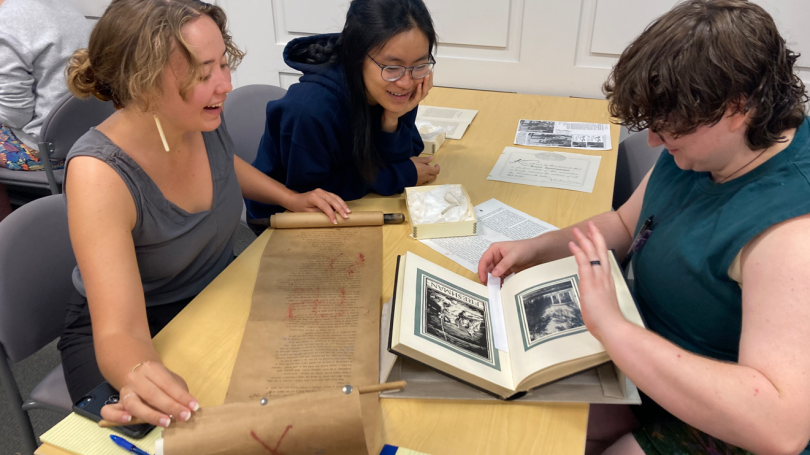 Three students sitting at a table looking at artifacts at the library. 