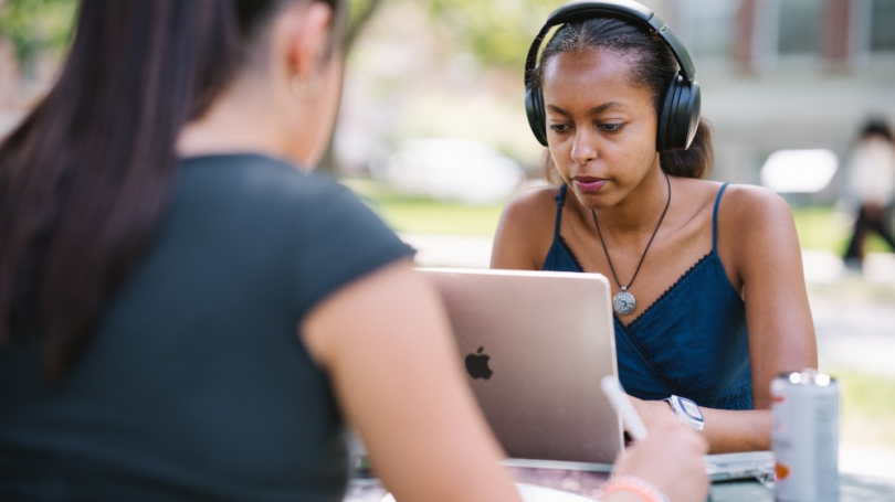 Student working outside on a laptop while wearing headphones