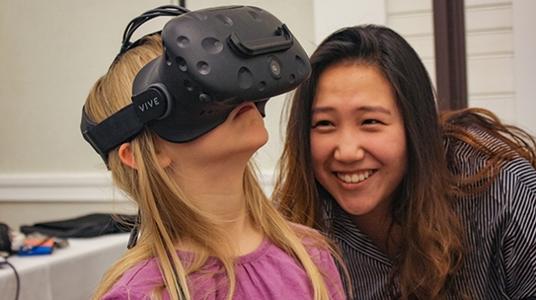 a woman watching a young girl trying out a virtual reality device