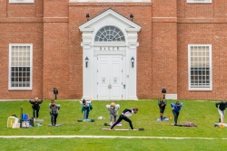 SWC Outdoor Yoga Class People practicing yoga on mats on green lawn in front of large brick building, Baker library