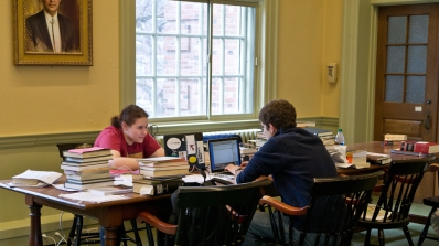 Two students sitting and studying with their books and computers.